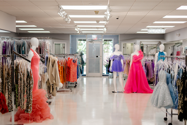inside Kotsovos dress store, dress racks full of colorful dresses and mannequins wearing a purple, red, and orange dress