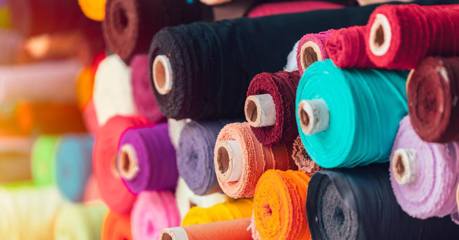 Rolls of solid-colored silk fabrics in black, pinks, oranges, purples, and reds stacked on top of each other.