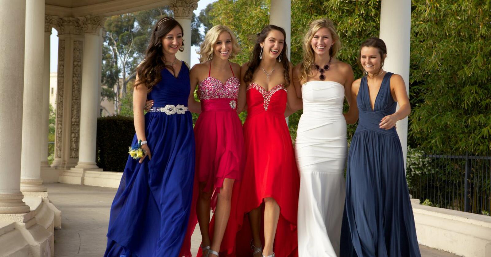 Four young women wearing formal dresses of varying colors and lengths smile and walk in a gazebo.